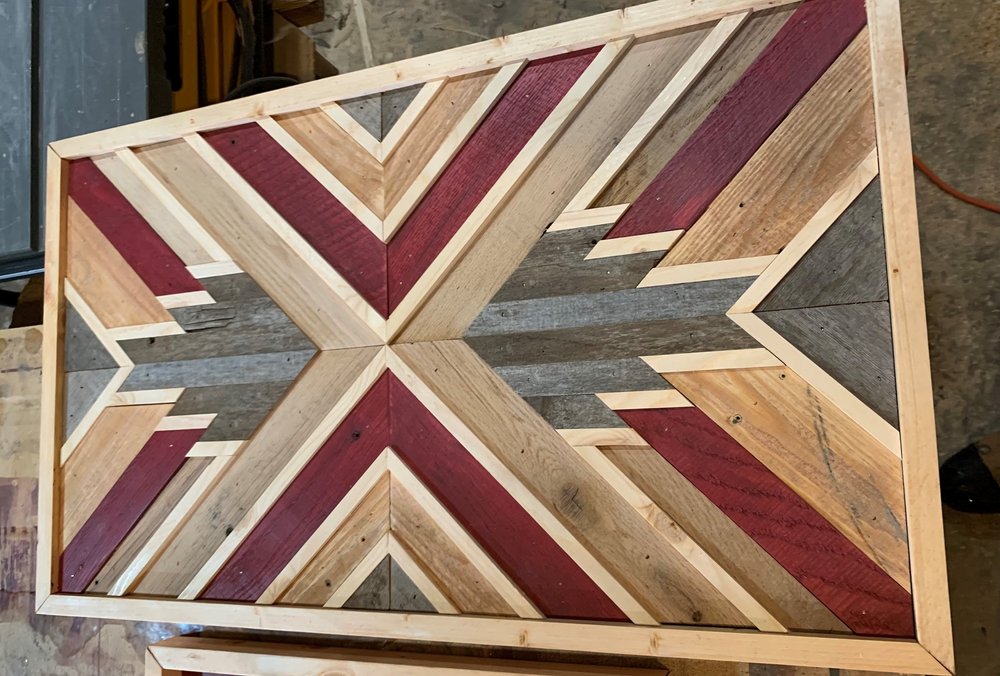 Top view of a handcrafted wooden table featuring a geometric chevron pattern in various shades of red, brown, and natural wood tones, showcasing skilled woodworking techniques and rustic design elements.