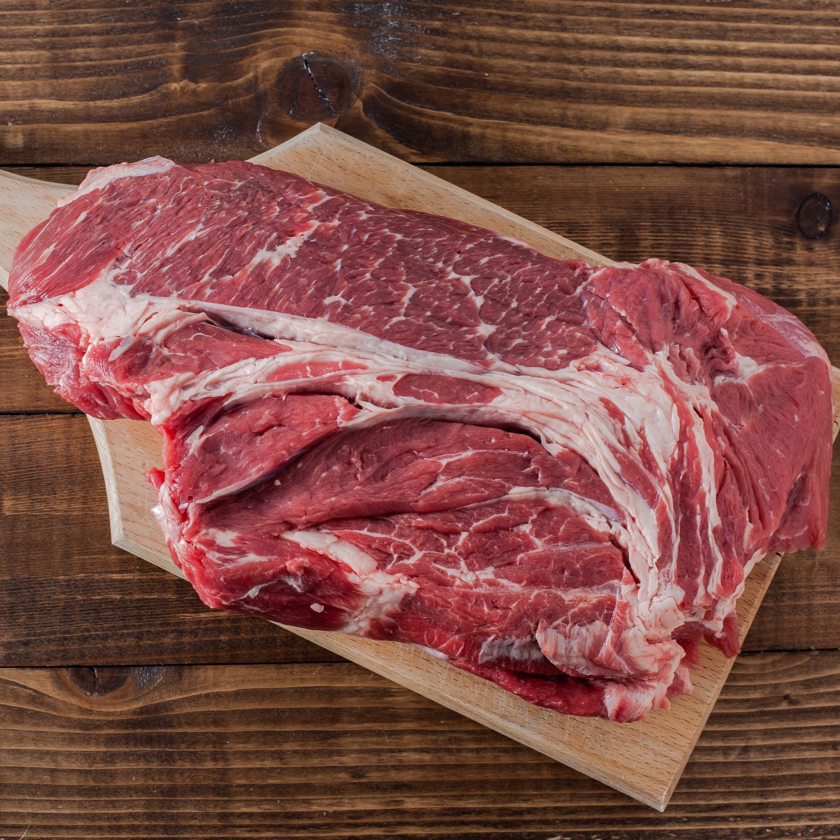 Raw beef chuck roast displayed on a wooden cutting board, showcasing marbling and rich red color, ideal for slow cooking and braising.