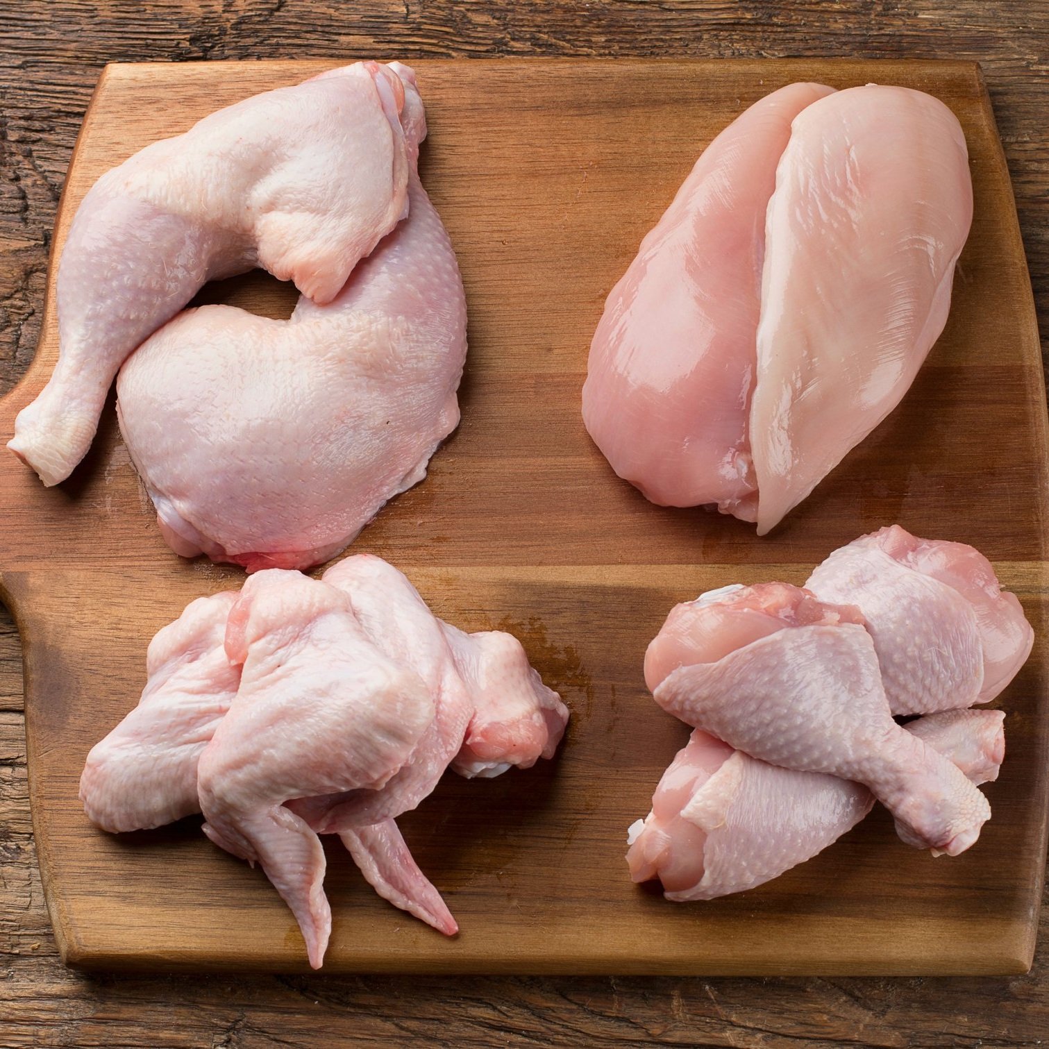 Raw chicken cuts displayed on a wooden cutting board, including chicken thighs, breasts, and wings, showcasing various parts for culinary use.